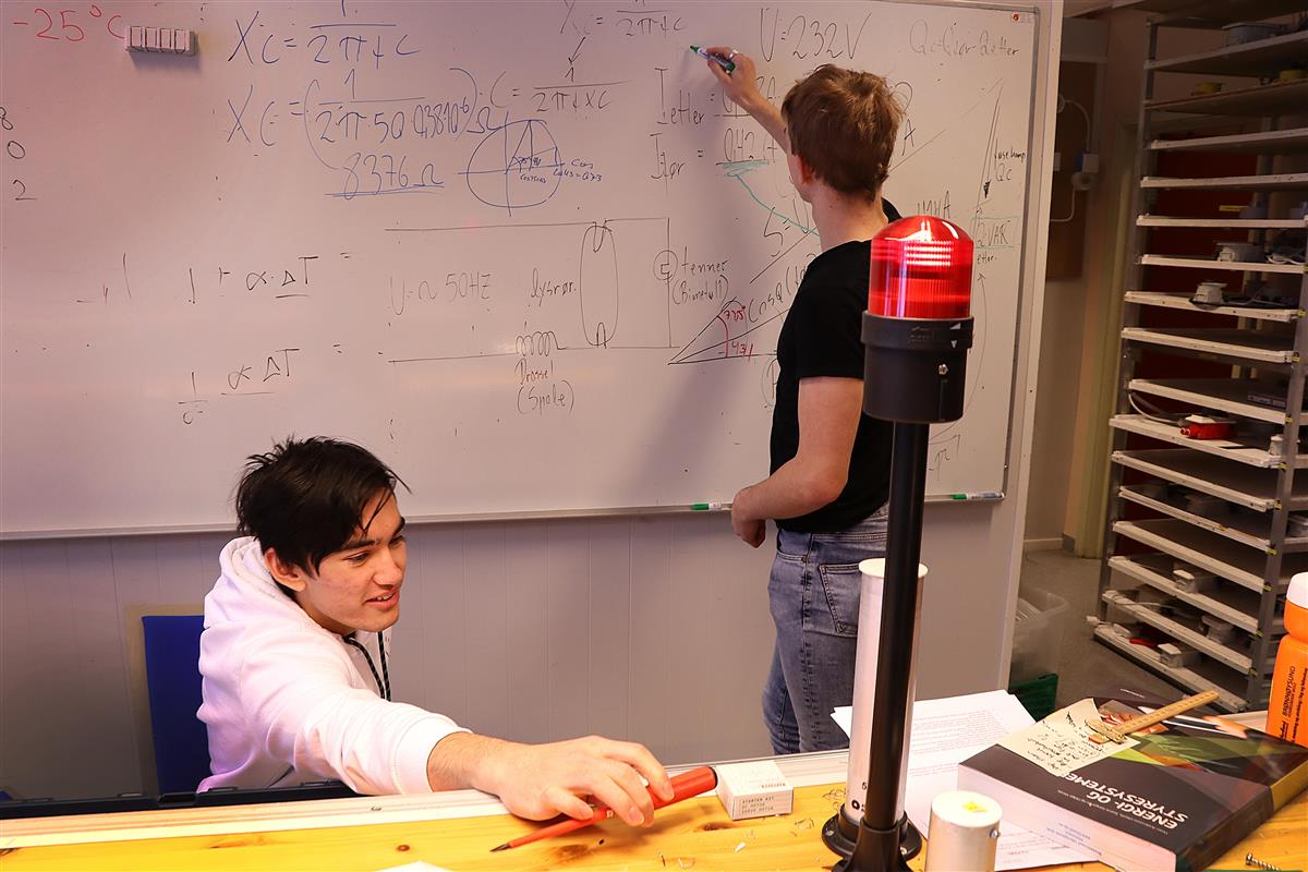 To elever på elektro-og datateknologi. Den ene eleven skriver på tavla, mens den andre holder et skrujern. - Klikk for stort bilde